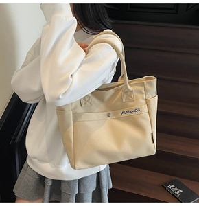 Detail of beige canvas tote bag showing the front pocket with snap and blue embroidery