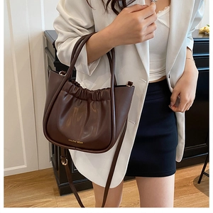 Detail of dark brown pleated bucket bag with gold lettering on white blazer model
