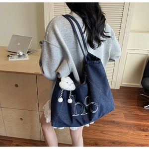 Detail of blue denim tote bag with white letter embroidery and a plush cloud charm