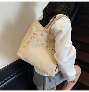 Detail of beige canvas tote bag with blue AIME embroidery and side metal button snaps