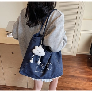 Detail of blue denim tote bag with white embroidery and cloud charm on model's shoulder