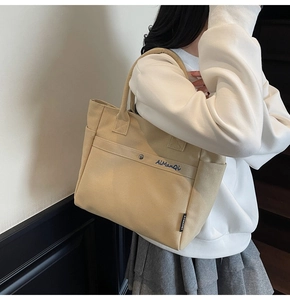 Close-up of the beige canvas tote bag side pocket with brand label and embroidery detail