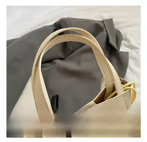 Détail de la poignée ergonomique en similicuir crème avec ruban noir sur un sac seau