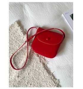 Détail d'un sac selle rouge brillant avec fermeture magnétique sur fond de tissu doux