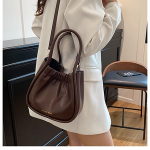 Detail view of dark brown pleated leather bucket bag with top handles and shoulder strap