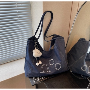 Detail of blue denim tote bag with white letter embroidery and plush cloud keychain charm