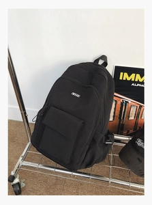 Detail view of the MYJC logo and front zip pocket on this black nylon travel backpack