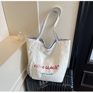 Detail of canvas tote bag with Crème Glacée embroidery and lace bow on luggage