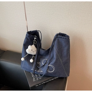 Close-up of dark blue denim tote bag with LSO lettering and white plush cloud pendant