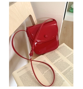 Détail d'un sac selle en cuir verni rouge posé sur une chaise en bois avec magazine