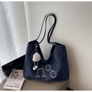 Close-up of a blue denim tote bag with white embroidery and a plush cloud charm