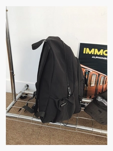 Side view of a black nylon backpack with drawstring pockets and multiple zippers