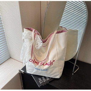 Detailed close-up of white canvas tote bag with Crème Glacée embroidery and lace ribbon