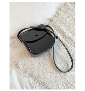 Vue de dessus d'un sac besace en cuir verni noir avec boucle ronde sur fond minimaliste