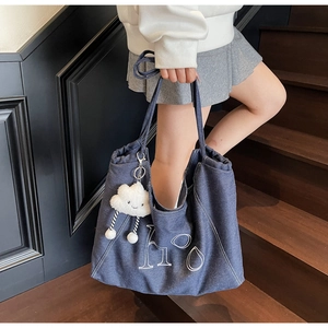 Detail of blue denim tote bag with white embroidered letters and cloud plush charm accessory