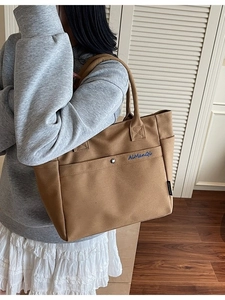 Khaki canvas tote bag with front pocket and blue embroidery on shoulder of model