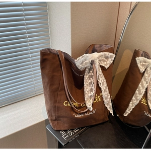 Detail of brown canvas tote bag with yellow embroidery and large white lace bow