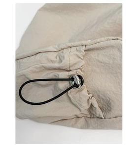 Detail view of beige nylon fabric with black elastic drawstring and silver metal toggle