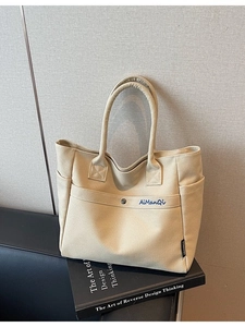 Minimalist beige canvas tote bag with embroidered logo on a stack of books