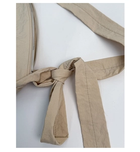 Detail of beige canvas crossbody bag with knotted strap and silver metal zipper closure