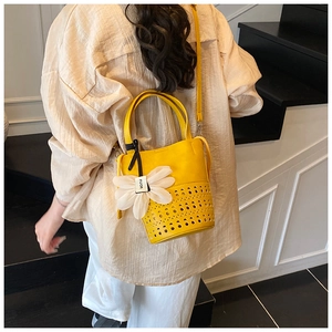 Détail du sac seau jaune vif avec motifs ajourés au laser et breloque marguerite blanche