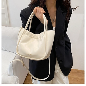 Detail of a creamy white pleated bucket bag with gold lettering shown on a model