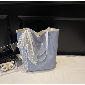Close-up of blue striped canvas tote bag with a white lace bow charm and brand patch
