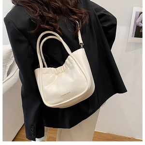 Close-up of beige pleated bucket bag with gold lettering shown in a stylish minimalist setting