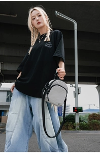 Gros plan sur un sac bandoulière en nylon gris porté avec un t-shirt noir et un jean