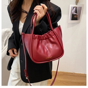 Detailed close-up of dark red pleated bucket bag with gold logo and fine stitching