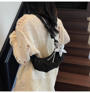 Detail of black crossbody bag with silver starfish charm and knotted leather strap on shoulder