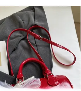 Détail d'un sac à main rouge avec chaîne de perles et nœud décoratif en tulle blanc