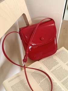 Sacoche selle rouge en cuir verni avec bouton pression suspendue à une chaise