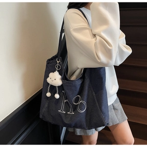 Detail of blue denim tote bag with white 'ho' embroidery and fluffy cloud pendant