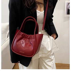 Close-up of wine red bucket bag featuring pleated top design and golden logo branding