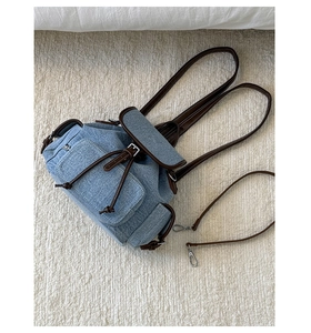 Detail of denim backpack showing drawstring closure and leather flap on plush rug background
