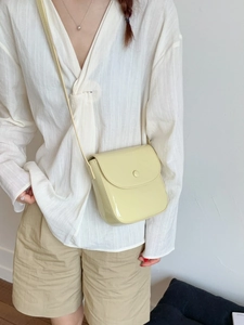 Sac à bandoulière minimaliste crème brillant porté par un mannequin en tenue d'été