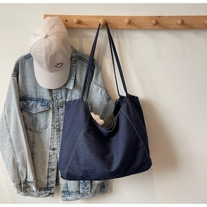 Detail of a large denim tote bag with contrast stitching and plush doll charm