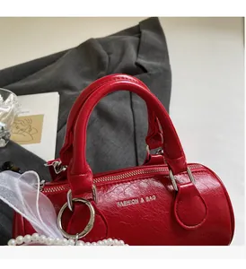 Détail du sac cylindrique en cuir rouge texturé avec anneaux argentés et poignée chic