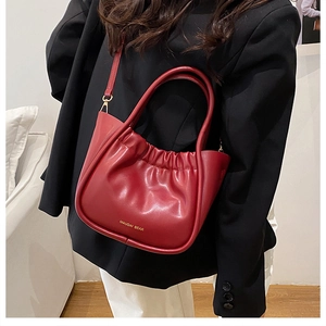 Detail of red pleated bucket bag with gold brand lettering and metallic hardware accents