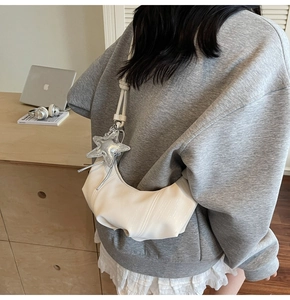 White crescent underarm bag with silver star pendant shown in a stylish urban setting