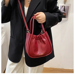 Deep red pleated bucket bag with gold lettering shown being carried by a model