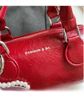 Détail du sac oreiller en cuir rouge avec perles, boucles argentées et texte mode