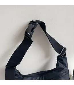 Detail of adjustable wide shoulder strap and plastic buckle on black nylon crossbody bag