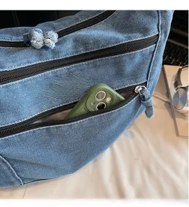 Detail of front zipper pocket on blue denim crossbody bag with space for smartphone