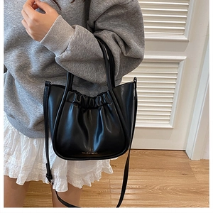 Close-up of black pleated bucket bag with gold logo and elegant top handle detail
