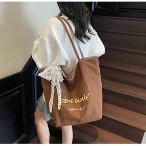 Detail of a brown canvas tote bag with French text and white lace ribbon on strap