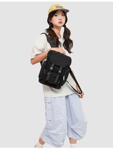 Detail of a black canvas backpack with dual buckle closure worn by a model in casual style