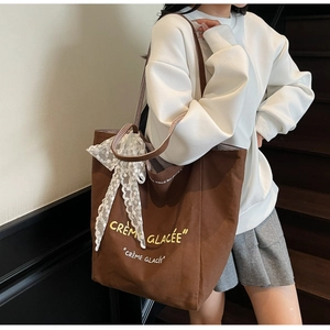 Detail of dark brown canvas tote bag with lace bow and striped handles on white hoodie