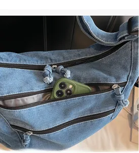 Detail view of denim crossbody bag showing multiple functional zipper pockets and inner space